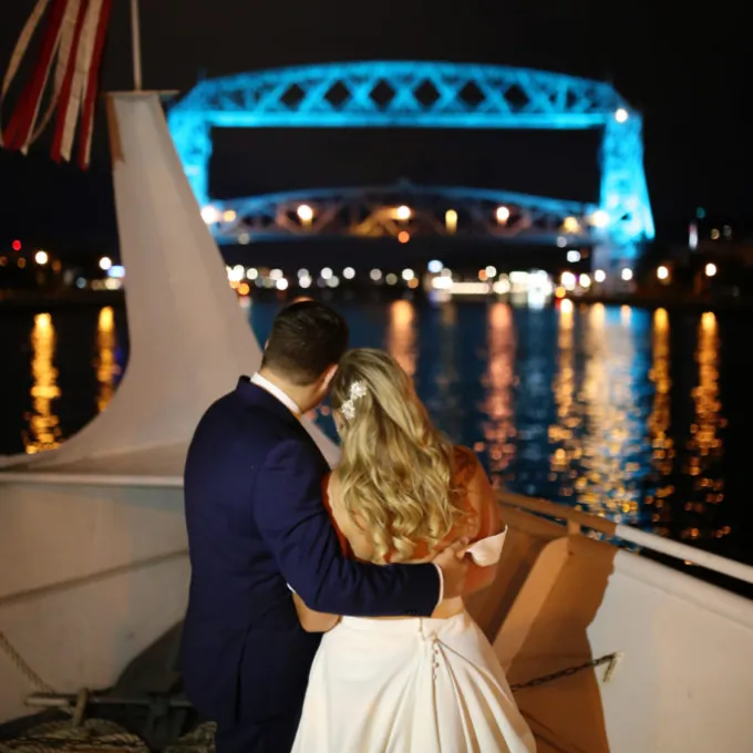 bride and groom on a boat looking at a bridge