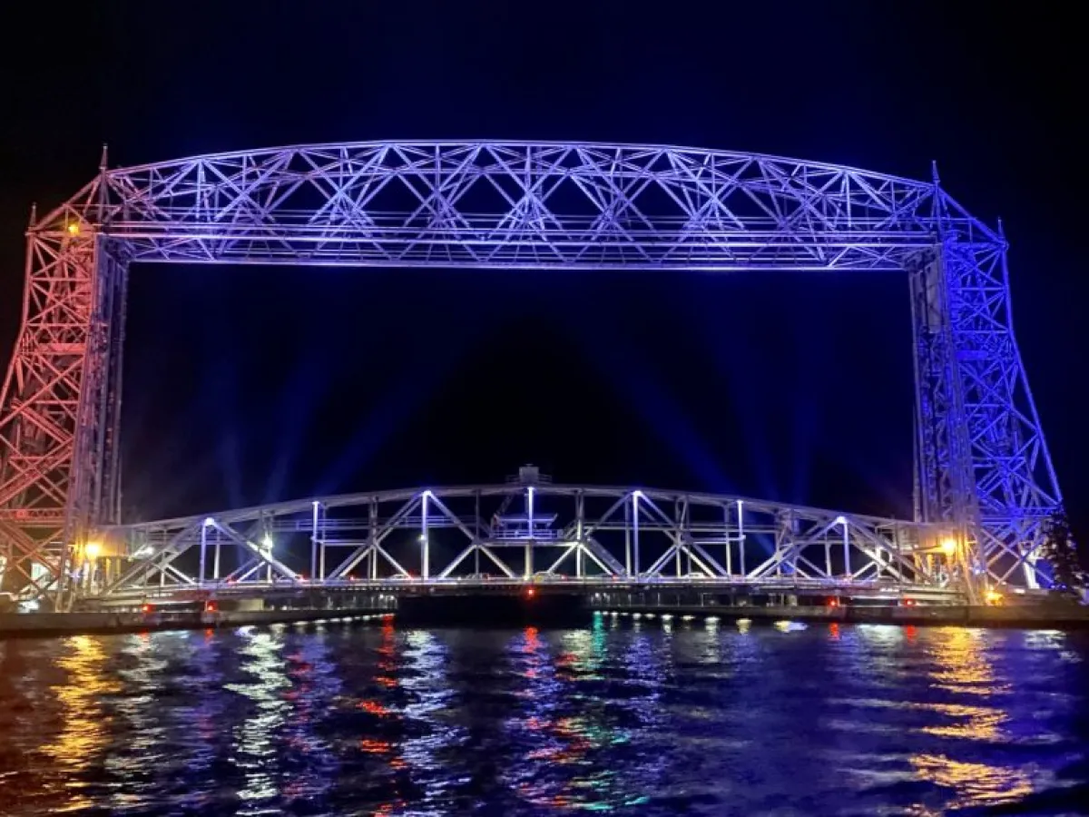 a large bridge lit up at night with Aerial Lift Bridge in the background