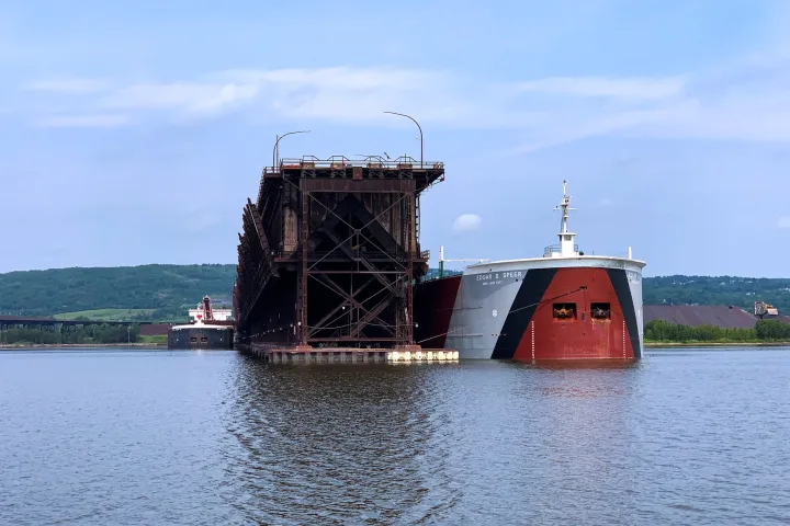 a large ship in a body of water with Holland Harbor Light in the background