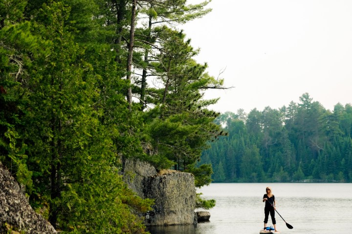 a man riding on the back of a boat next to a lake