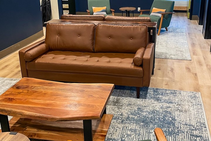 Modern lounge with brown leather sofa, green chairs, and wooden tables on patterned rugs.