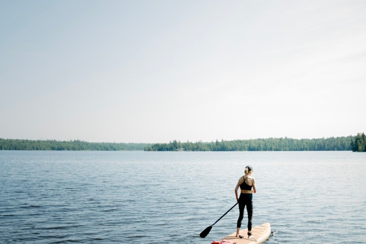 Person paddleboarding on a calm lake under clear sky.