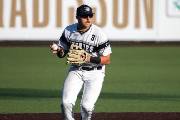 Baseball player in white uniform preparing to throw ball on field.