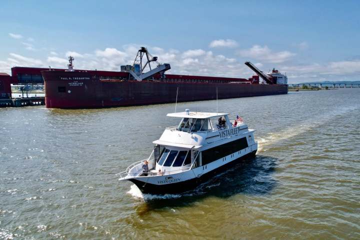 Vista Queen cruising past a large cargo ship on a sunny day.